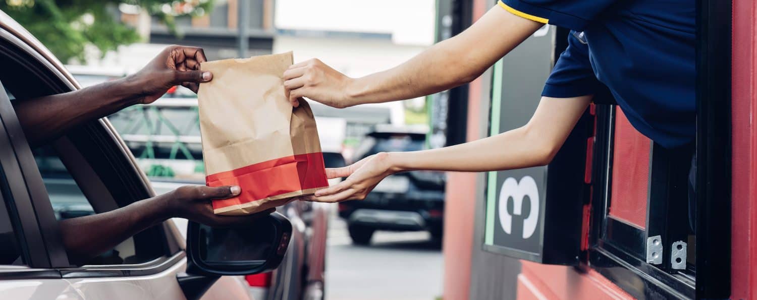 Hand Man in car receiving coffee in drive thru fast food restaurant. Staff serving takeaway order for driver in delivery window. Drive through and takeaway for buy fast food for protect covid19.