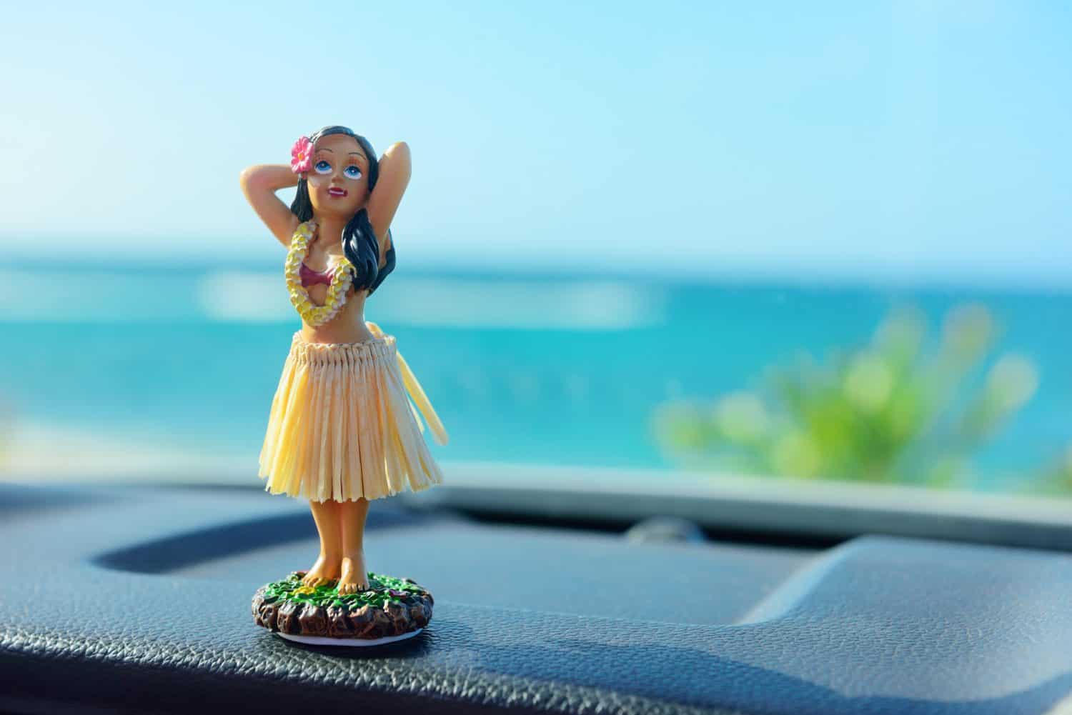 Hawaii road trip - car hula dancer doll dancing on the dashboard in front of the ocean. Tourism and travel freedom concept.