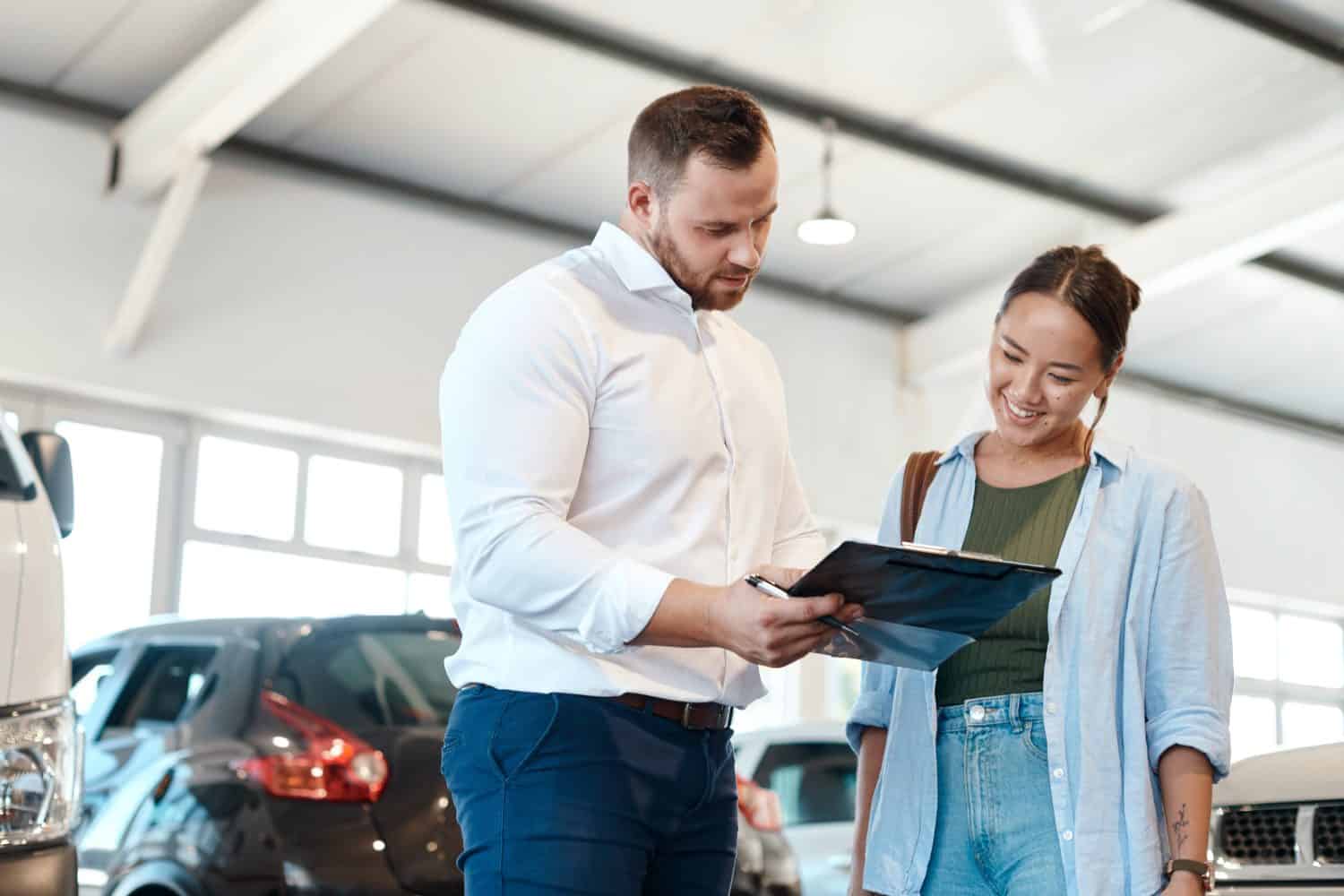 Car, dealership or documents with salesman and customer in showroom for conversation, deal or offer. Contract, finance or insurance with agent and asian woman in discussion for vehicle purchase