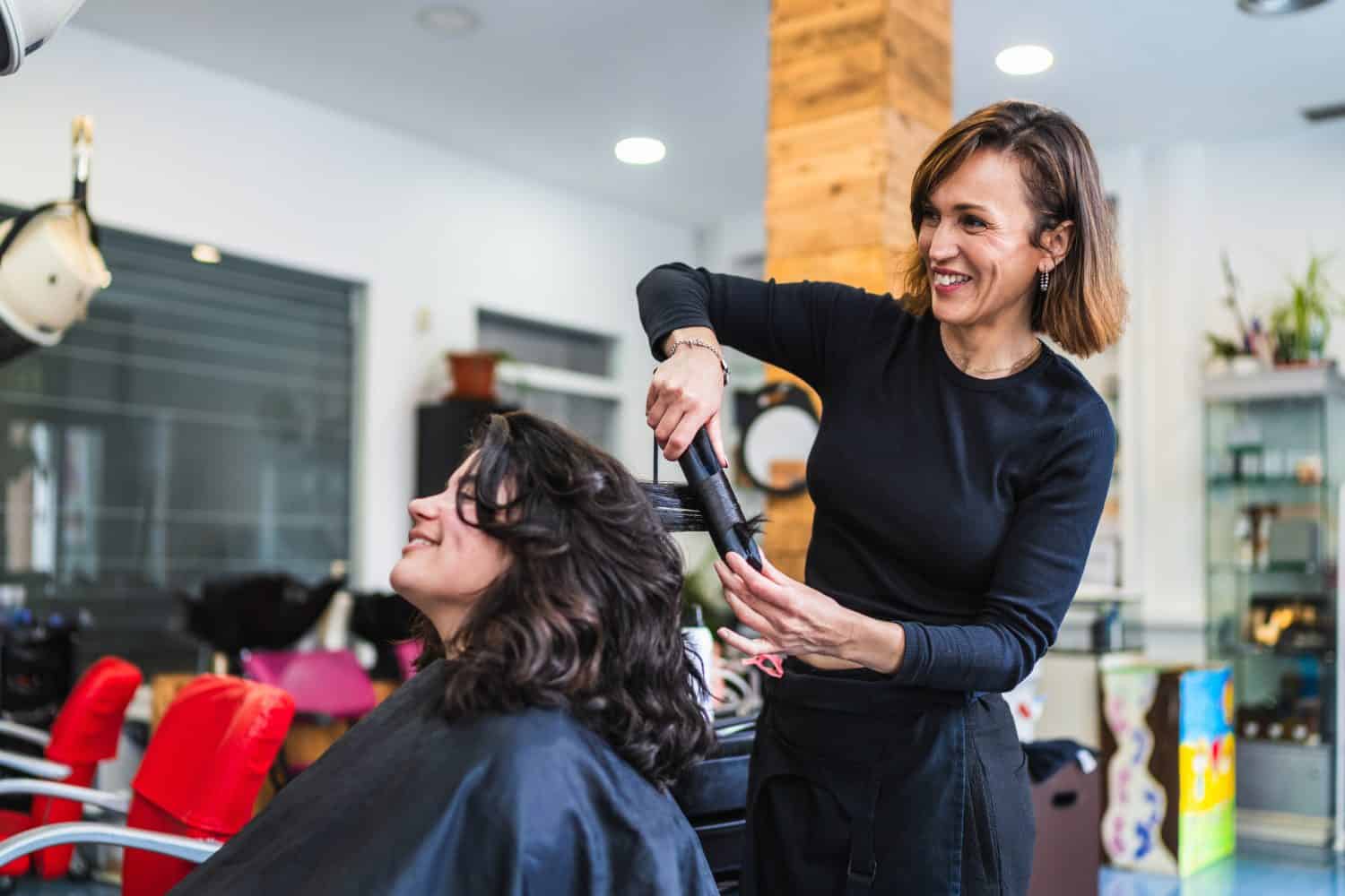 A hairdresser uses a curling iron to curl a client's hair in a modern salon. The setting is professional and stylish. Concept of professional hair curling.