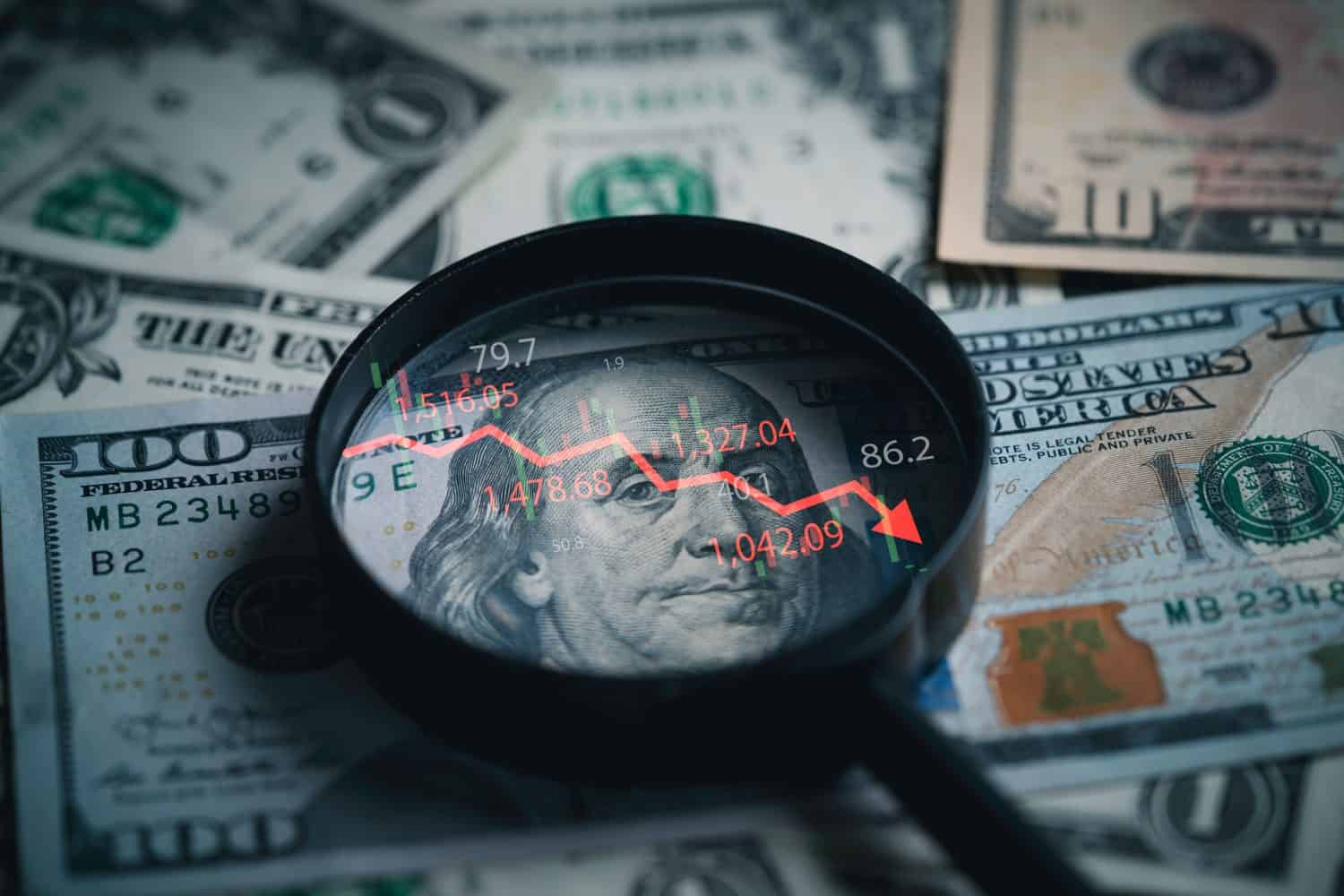 Red down arrow inside of magnifier glass and USD dollar banknote for United States of America or USA economic recession concept.