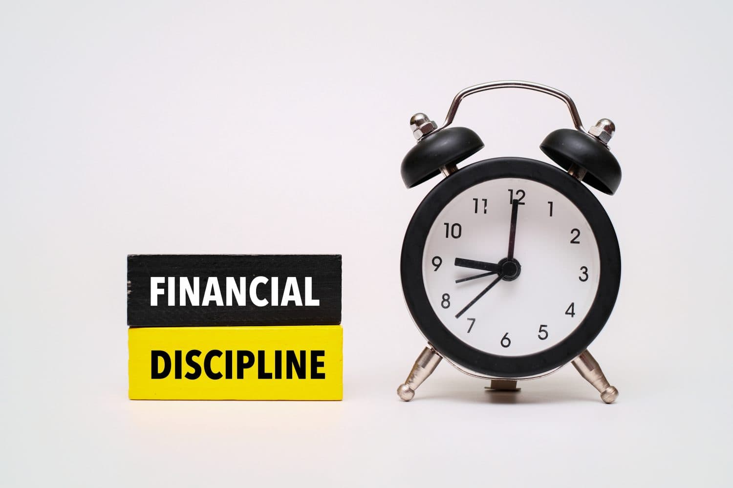 A coloured wooden block with text FINANCIAL DISCIPLINE on it next to black alarm clock