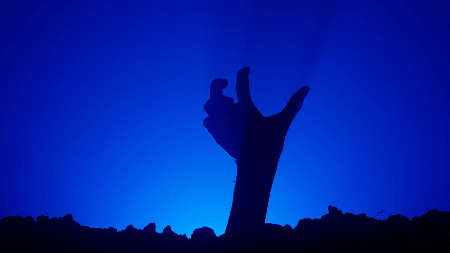 Scary dirty halloween zombie hand silhouette raising up from grave crawling and moving fingers, isolated on blue background. Mystery halloween concept.