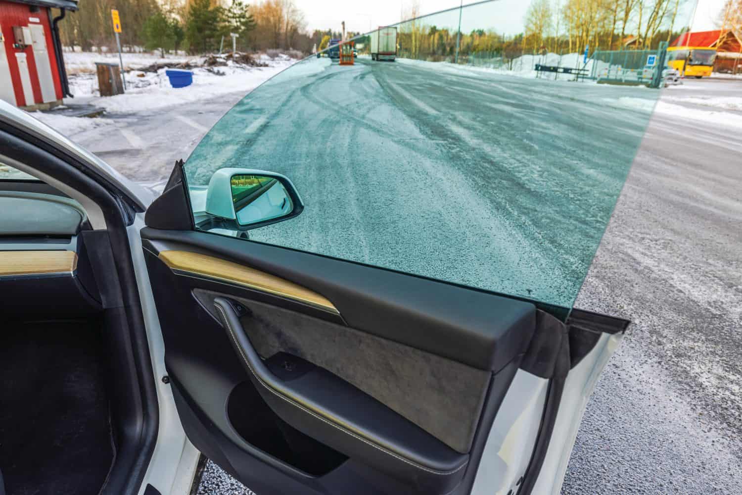 Open car door of Tesla Model Y revealing modern interior design and clear glass window against snowy backdrop. Sweden.