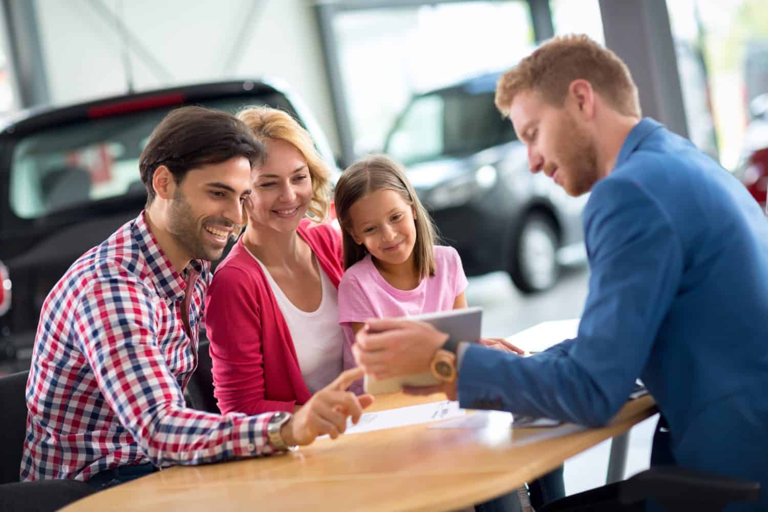 Happy family in car dealership choosing their new car, friendly car agent helping