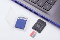 MicroSD memory card with adapter near the SD port of the modern blue laptop. One more blue SD memory card in a transparent case lays near the computer.