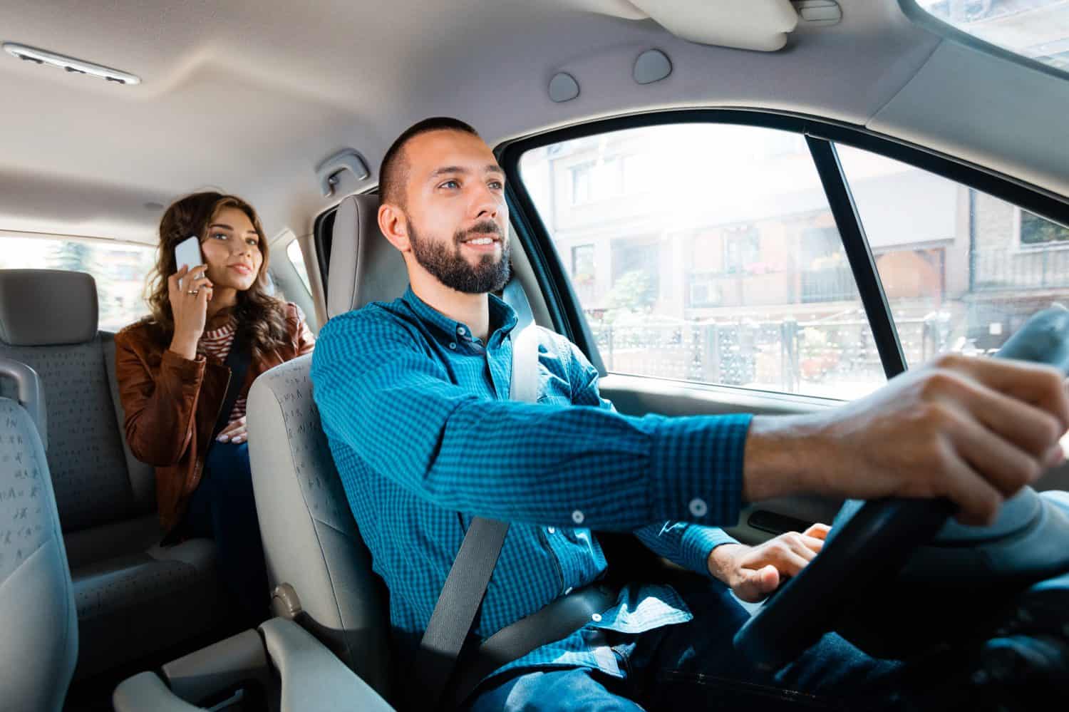 Smiling driver talking with female passenger. Woman using mobile phone in the background.