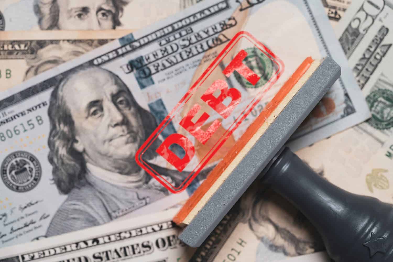 Red stamp debt wording on Benjamin Franklin of one hundred American USD banknote for United States of America government debt ceiling concept.