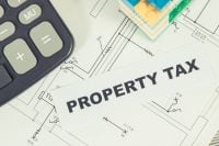 Inscription property tax with small house made of colorful toy blocks and calculator. Increasing real estate or luxury taxation. Tax payments