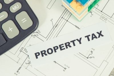 Inscription property tax with small house made of colorful toy blocks and calculator. Increasing real estate or luxury taxation. Tax payments