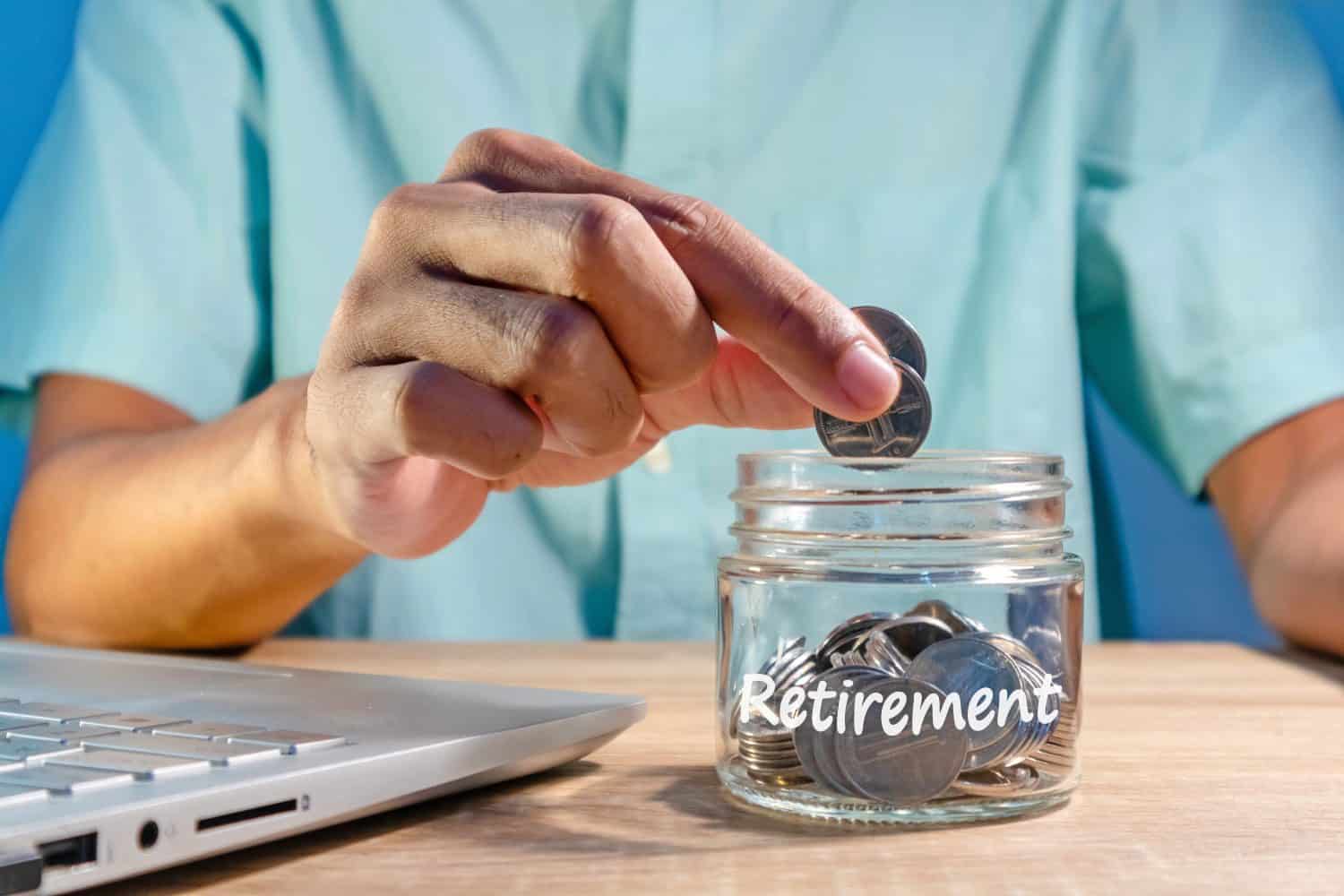 Man working with a laptop and putting coins into a glass jar to prepare for retirement. Saving money for retirement.