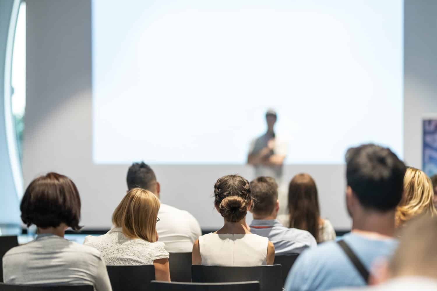 Male speaker giving a talk in conference hall at business event. Audience at the conference hall. Business and Entrepreneurship concept. Focus on unrecognizable people in audience.