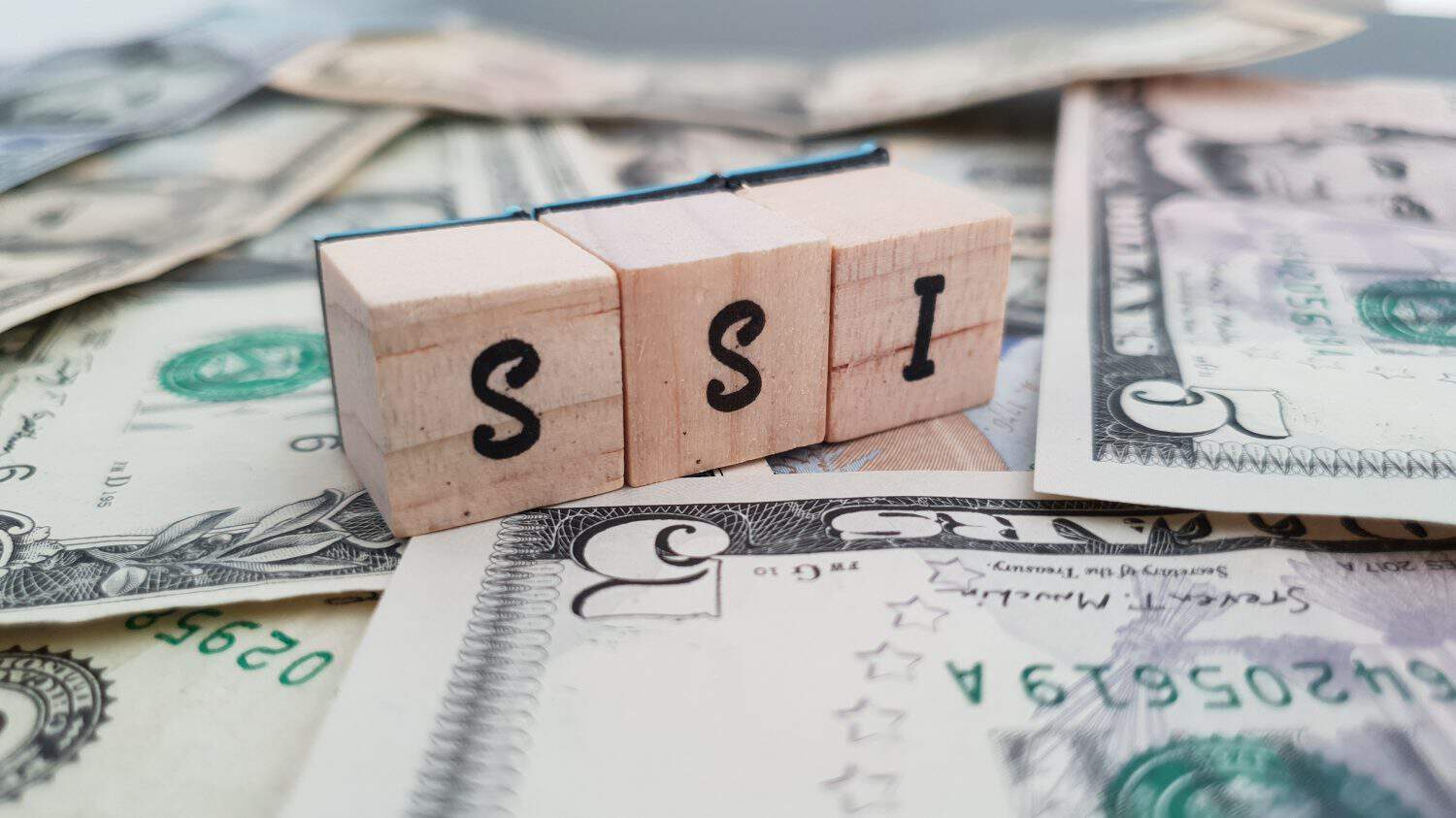 SSI acronym made of wooden letter cubes on pile of US dollar banknotes. Supplemental Security Income