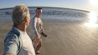 Mature couple walk along empty beach, hold hands