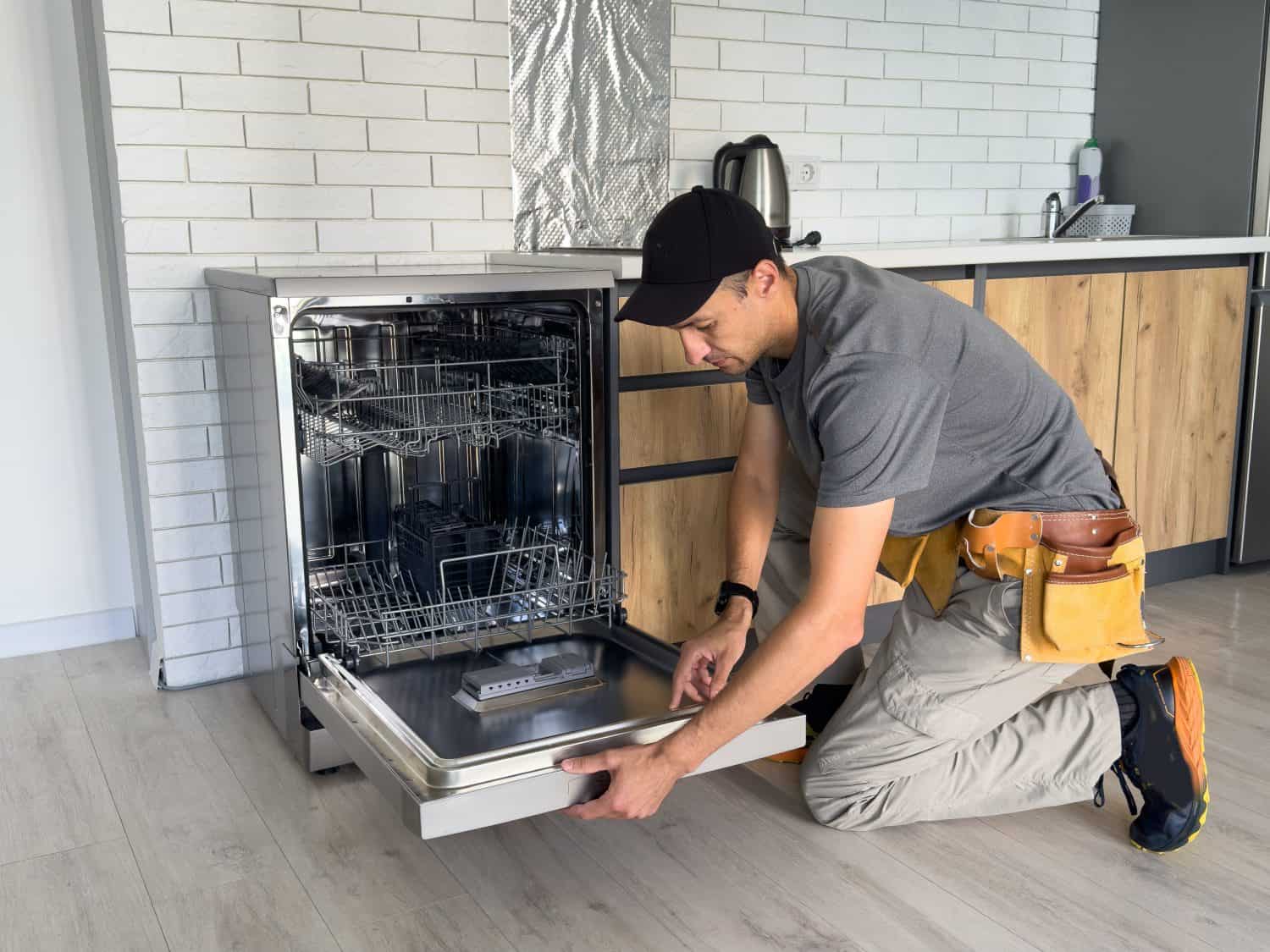 Young Repairman Service Worker Repairing Dishwasher Appliance In Kitchen