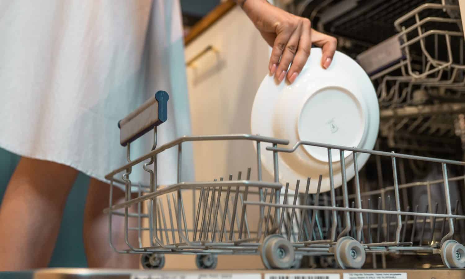 Woman loads plates to dishwasher machine. Daily routine concept.
