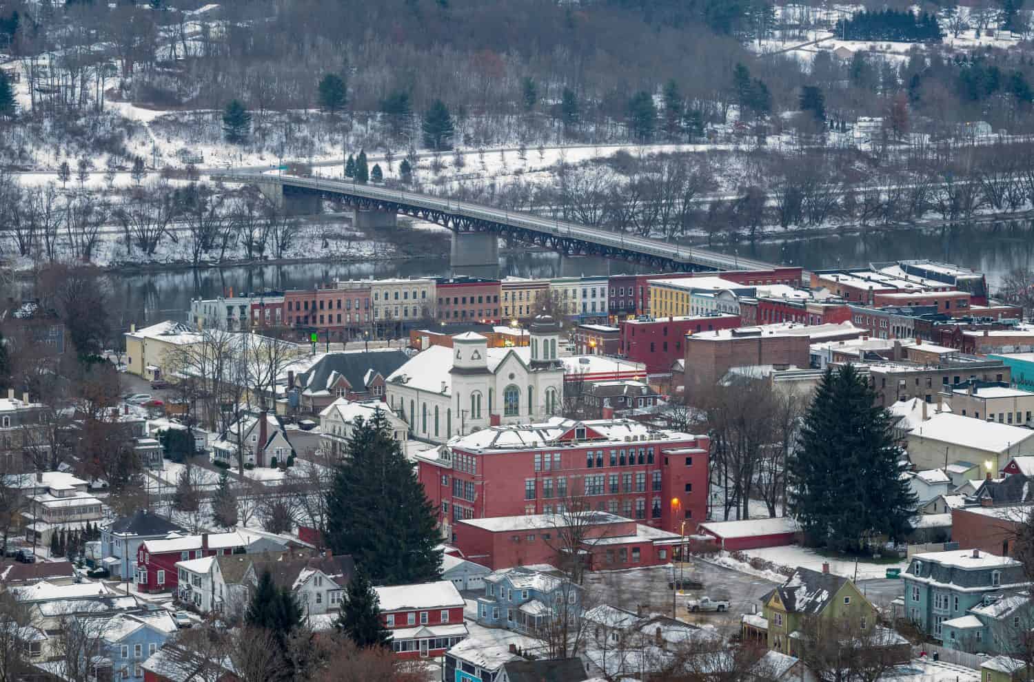 Owego is a small village in New York State, located along the Susquehanna River, photographed from the top of a hill during a winter morning with fresh snow on rooftops .