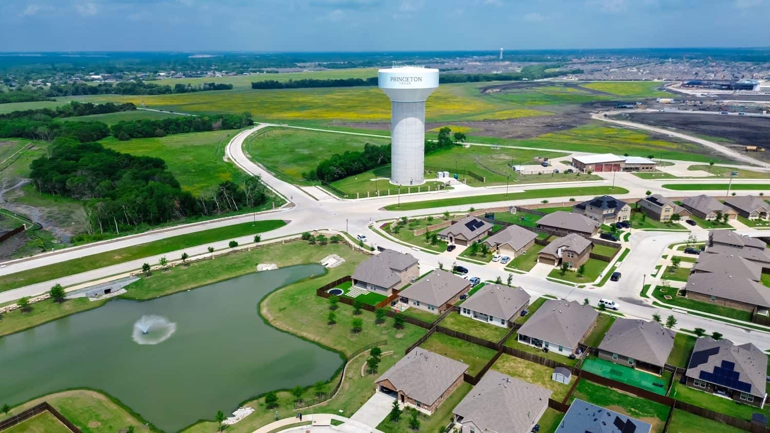 Lakeside two story houses with fountain, water tower along Myrick Lane in Princeton, Texas, slab foundation site preparing, upscale solar roofing on new construction home large backyard, aerial. USA