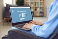 Young businesswoman or student girl sitting in armchair at home using laptop to visit online bank website and open personal or business account. Hands and computer closeup. Safe money transfer concept