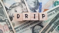 DRIP acronym made of wooden letter cubes on pile of US dollar banknotes. Dividend Reinvestment Plan