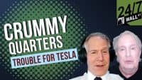 A financial news graphic features two men, one wearing headphones, discussing 'CRUMMY QUARTERS' and 'TROUBLE FOR TESLA.' The background has a green and dark blue patterned design, and a '24/7 WALL ST' logo is visible in the top right corner.