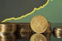 Golden XRP coins are displayed in front of green and blue financial graphs representing market trends and cryptocurrency fluctuations in a modern setting.