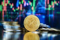 Piles of gold-colored Xrp coins take center stage. A digital graph in the background shows trends and fluctuating market data.