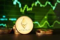A close-up shot of multiple gold Ethereum coins on a dark surface, with one large coin in the foreground showing the Ethereum logo and text. In the blurred green background, upward-trending financial graphs are visible.