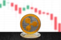 Ripple XRP on cryptocurrency coin with falling crashing graph on white background. The cryptocurrency coin is golden and in focus. This is a price concept of Ripple down market.