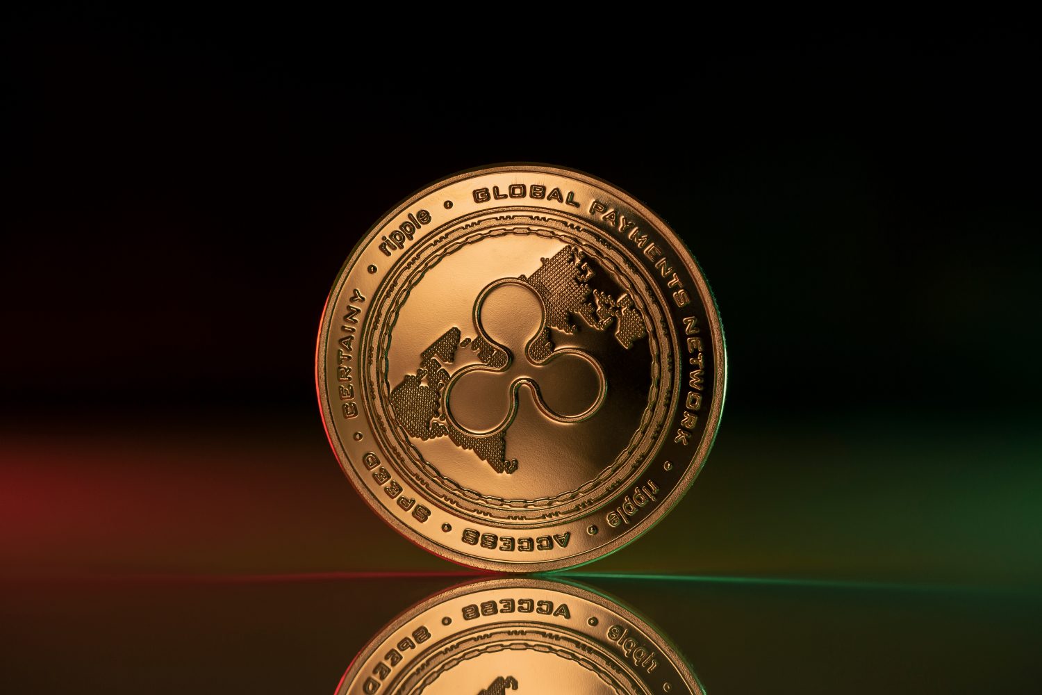 Ripple XRP cryptocurrency physical coin placed on reflective surface and lit with green and red lights