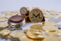 Cryptocurrency concept. Shining Monero cryptocurrency coin in front of five gold bars and by an old vintage pocket watch, isolated in white background. selective focus.