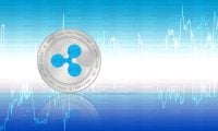 A silver Ripple (XRP) cryptocurrency coin with a blue, patterned ripple logo in the center is positioned in the foreground. The coin features 'RIPPLE • COIN • XRP • PEER TO PEER' inscribed around its edge. The background is a digital display of light blue and white financial charts, including line graphs and numeric data indicating cryptocurrency price movements and percentages, all against a gradient blue backdrop.
