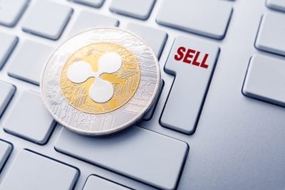A silver and gold Ripple (XRP) cryptocurrency coin rests on a light gray computer keyboard. To the right of the coin, a rectangular key is visible, featuring the word 'SELL' in bright red capital letters. The background shows several other light gray keyboard keys.