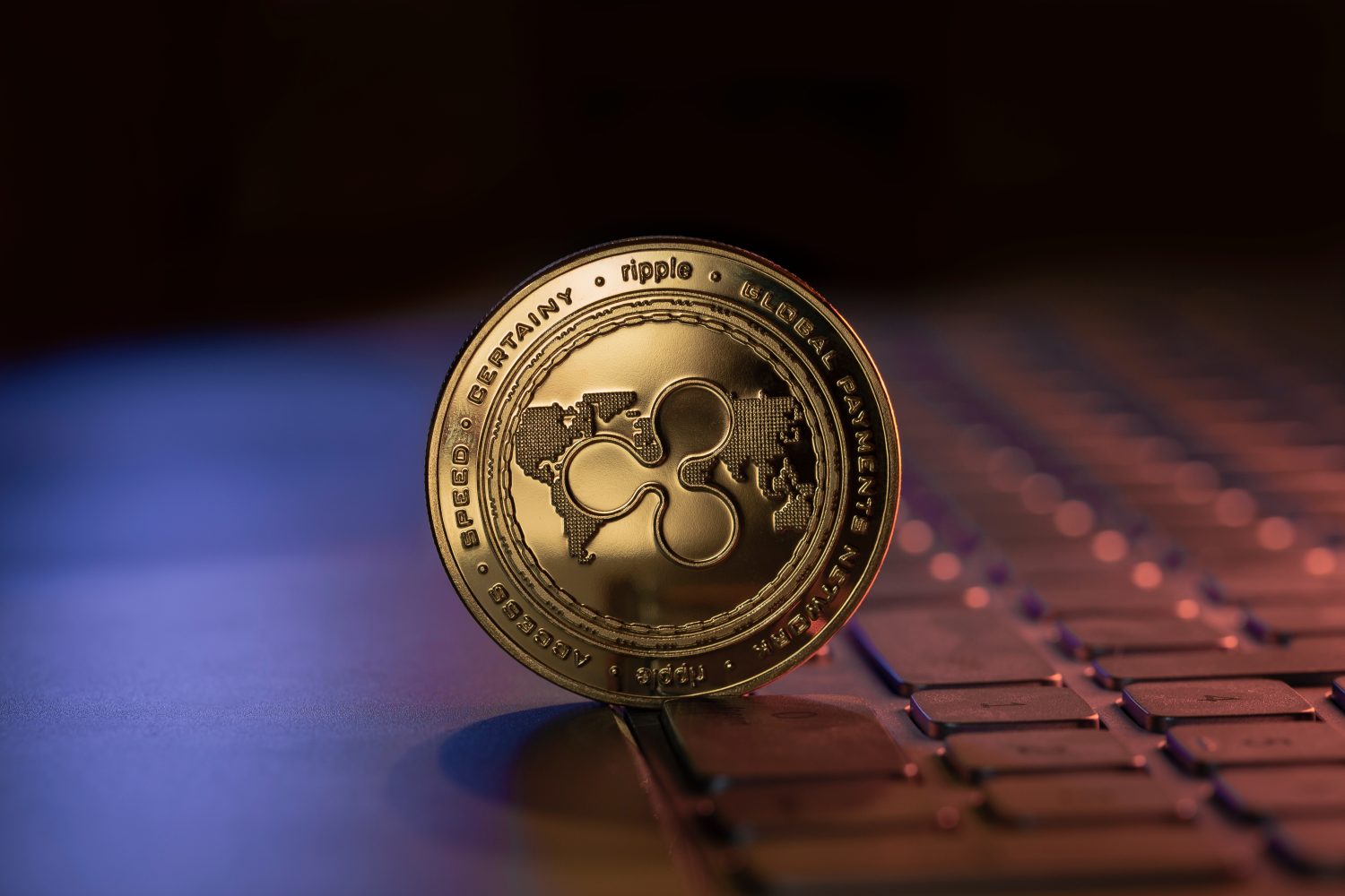 Ripple XRP cryptocurrency physical coin placed on laptop keyboard and lit with blue and purple lights