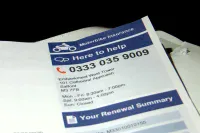 A white document with a prominent blue header labeled 'Motorbike Insurance' is visible against a dark background. The document, angled slightly, displays a phone number '0333 035 9009', an address for 'Embankment West Tower' in 'Salford, M3 7FB', and operating hours. Towards the bottom, a section titled 'Your Renewal Summary' is partially visible.