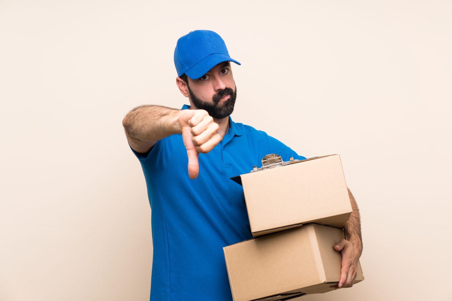 Delivery man with beard over isolated background showing thumb down with negative expression