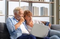 Senior couple spending time together in the living room, woman and man using laptop and digital tablet on the cozy sofa at home