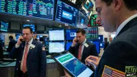 A busy trading floor features several male traders in suits, surrounded by multiple large electronic display screens showing stock market data and charts. In the foreground, a man in a navy suit with an American flag patch on his sleeve holds a black tablet, which displays a green 'COPY TRADE' button and a stock chart for 'NANC ETF'. Another trader in the mid-ground is on a phone, looking towards the left.
