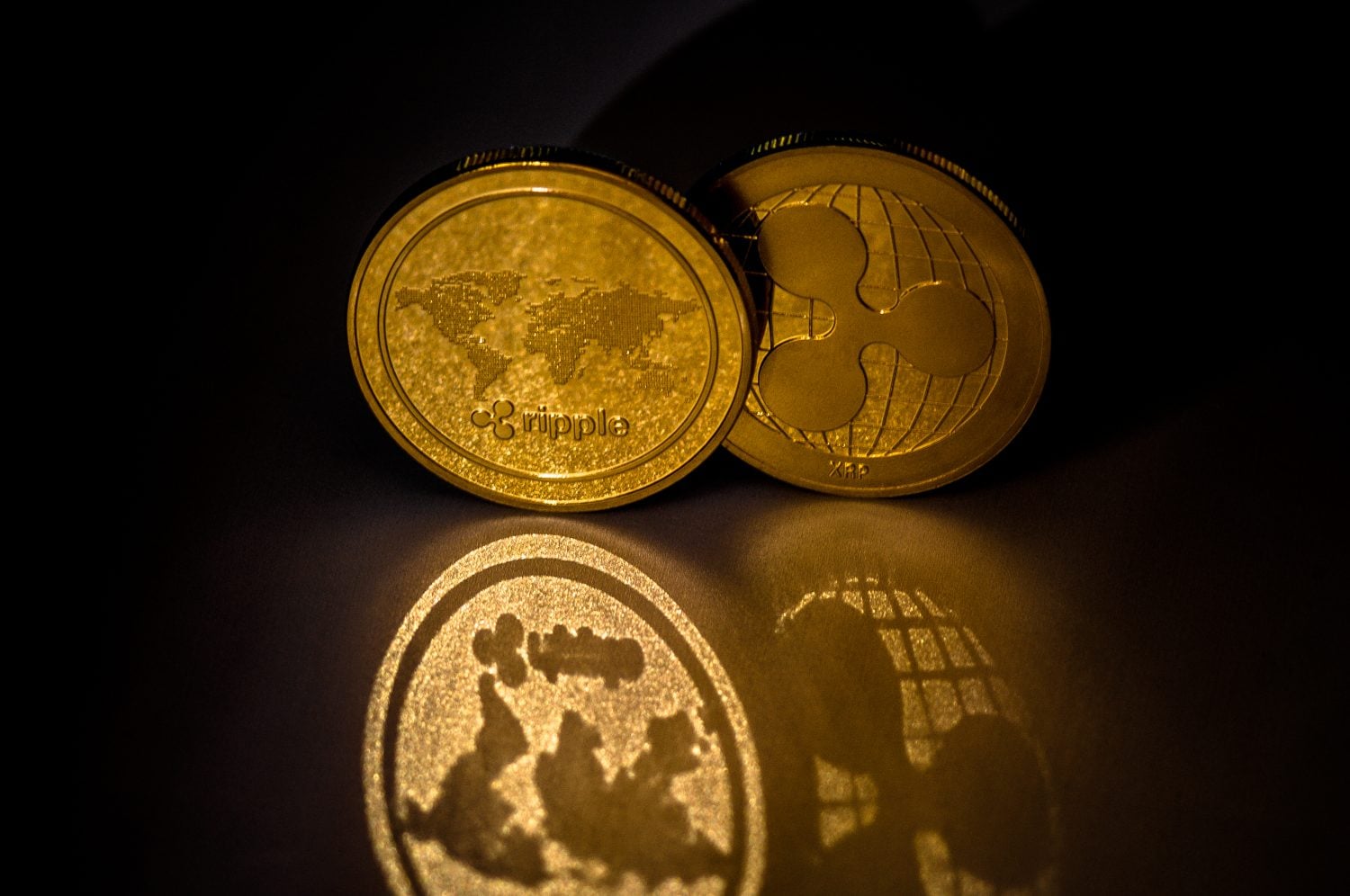 Shiny Golden XRP cryptocurrency coins on dark background with reflection