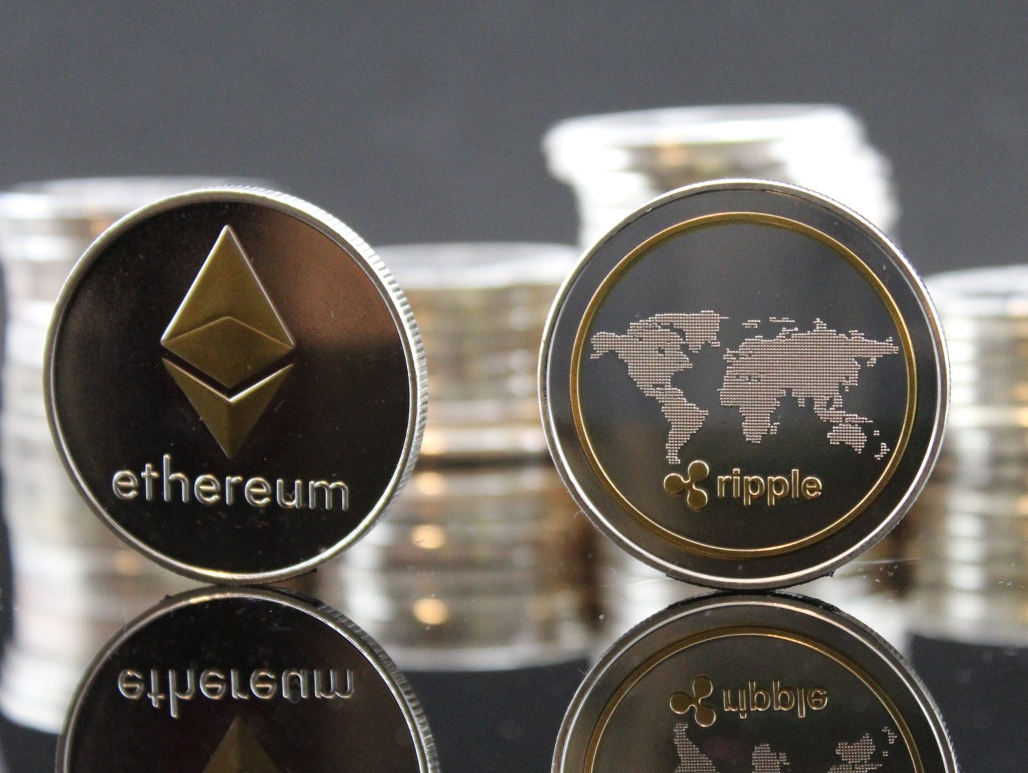 Ethereum ETH &amp; Ripple XRP coins with cryptocurrency stacks in the background