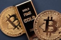 A large, rectangular, shiny gold bar with '999.9 FINE GOLD' embossed on its surface. It is centrally placed, with two round, golden Bitcoin coins partially visible on either side, each featuring the distinct 'B' logo and circuit board patterns. The background is a muted, dark blue.