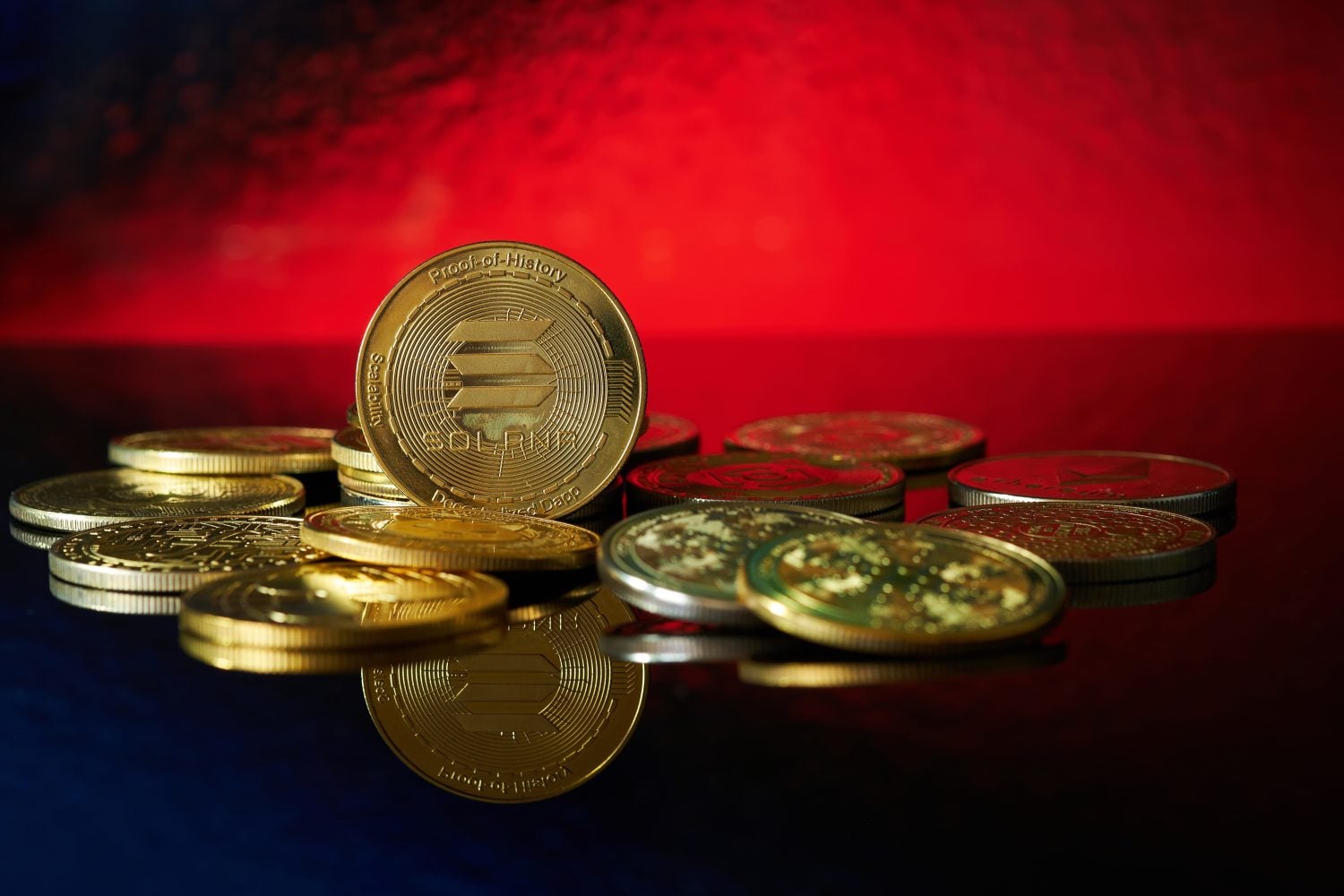 Close-up of golden Solana cryptocurrency rolled up with more cryptocurrencies on a reflective surface, highlighting its details against a striking red background.
