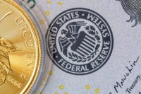 The Federal Reserve (Fed) logo on a dollar bill next to a one-ounce gold coin, symbolizing the concept of a stable currency value in relation to gold and the gold price.