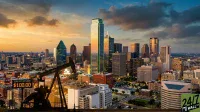 An aerial view of a vibrant cityscape at sunset, featuring a dark silhouette of an oil pumpjack in the foreground. A digital sign attached to the pumpjack reads 'BRENT CRUDE $100.00'. The city skyline is dominated by tall skyscrapers, illuminated by the warm glow of the setting sun and artificial lights. The sky transitions from a deep blue at the top to a golden orange near the horizon, with scattered clouds. A '24/7 WALL ST' logo is visible in the bottom right corner.