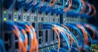 A detailed shot of server hardware with rows of blue and orange fiber optic cables plugged into networking ports with glowing indicator lights.