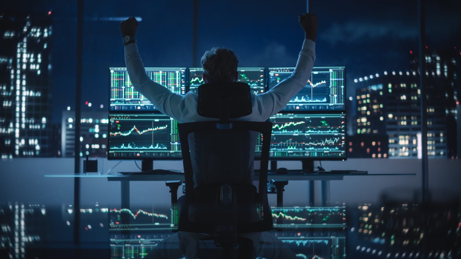 Stock Market Broker Working on a Computer with Multi-Monitor Workstation with Real-Time Investment, Commodities and Foreign Exchange Charts. Successful Businessman Punches Air for Winning a Trade.