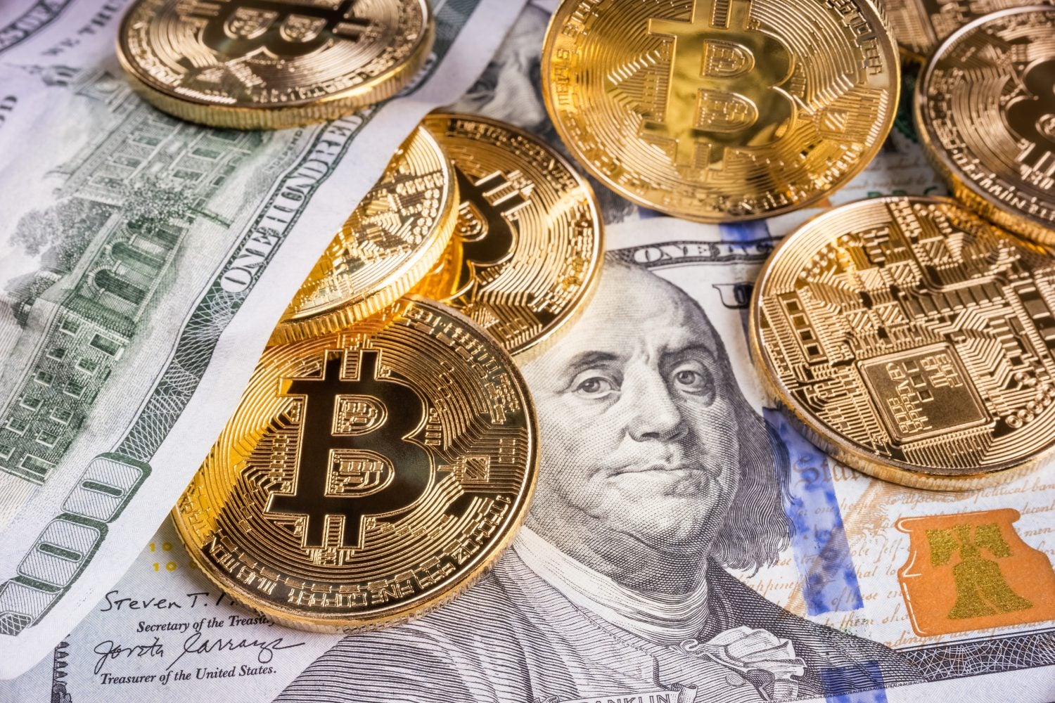 Crypto Bitcoin One dollar bitcoin, virtual money and one hundred dollar banknotes. Bitcoins on US dollars. Dollar to bitcoin exchange. Background with crypto bitcoins, and dollars. Golden bitcoin.