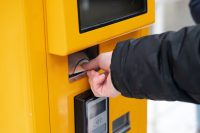 Closeup hand inserting card into yellow kiosk, commuter tapping contactless payment at metro station, gloved sleeve visible, focus on slot and card edge,