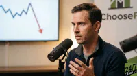 A man with short dark hair, wearing a navy blue quarter-zip sweater, speaks into a black Shure microphone. His left hand is raised in a gesturing motion, and he wears a wedding band. In the blurred background, a white screen displays a line graph with a blue zigzag line and a large red arrow pointing diagonally downwards. To the right, a white sign with a green logo reads 'ChooseFI'.