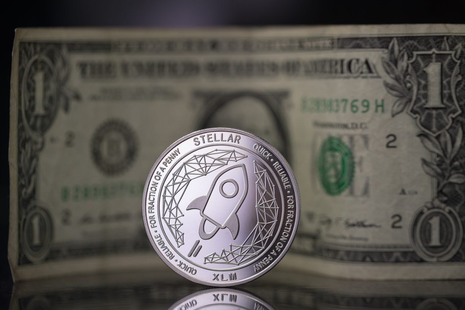 Stellar XLM cryptocurrency physical coin placed next to one dollar note in the black background